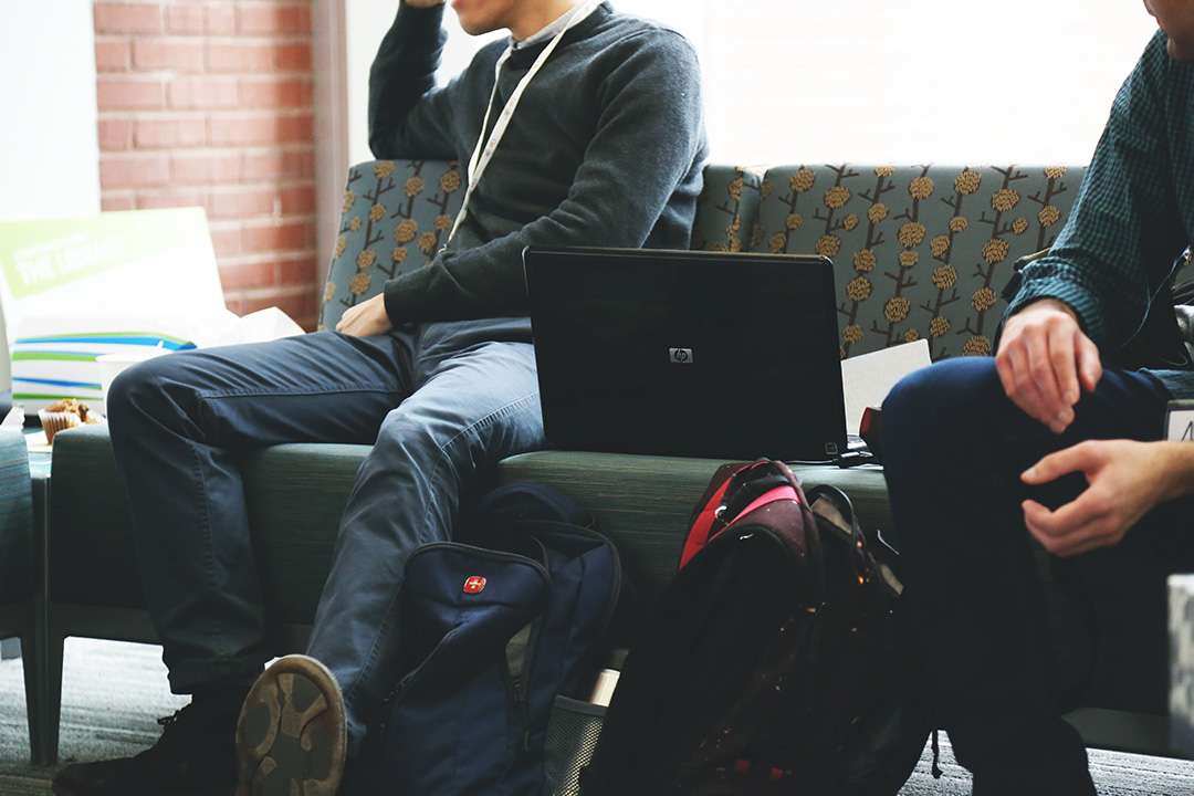 Two coworkers sitting on couch with laptop and backpacks