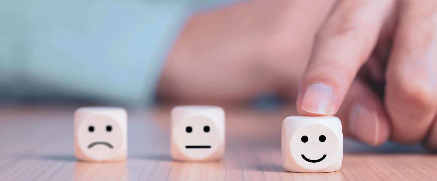 Three dice, one each with a frowny face (left), neutral face (middle) and smiley face (right)