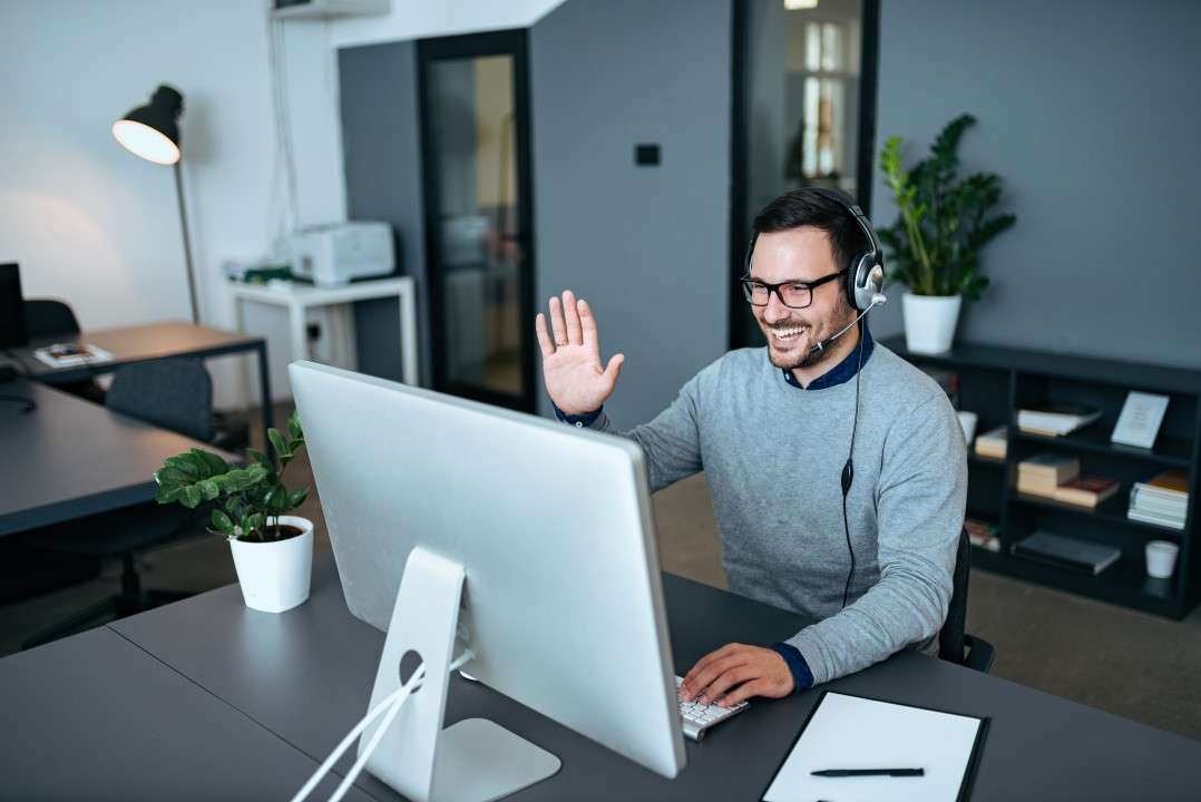 A remote worker waving to the screen on a video call.