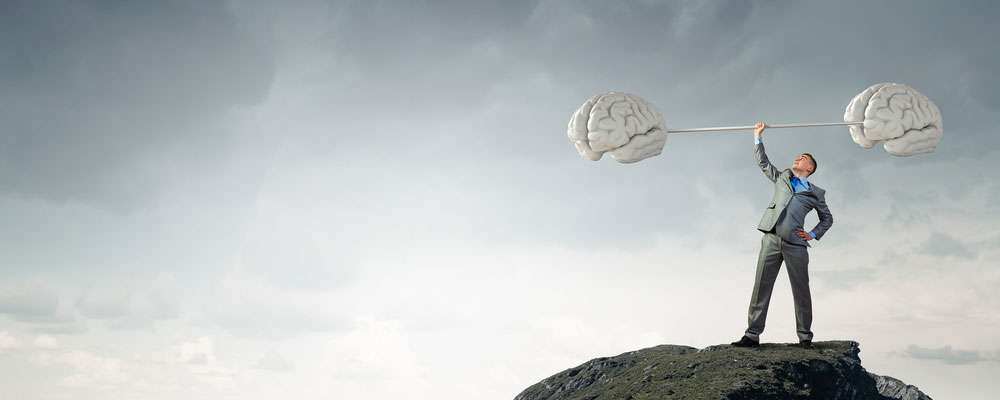 Man on cliff lifting a large brain shaped dumbbell into the air 