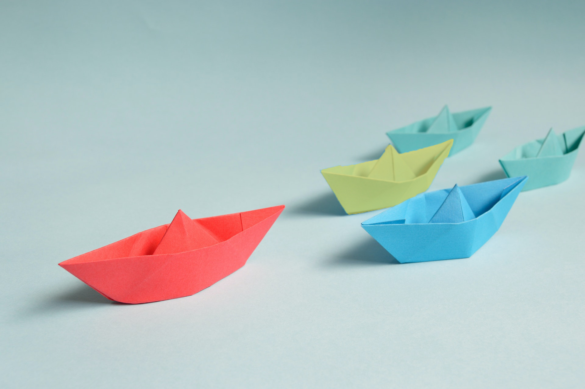 5 paper ships in red, yellow, blue and green navigating on a plain background - resilient leadership development programs help organizations navigate change with stronger team management